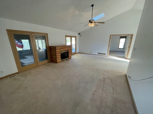 unfurnished living room featuring a skylight, ceiling fan, high vaulted ceiling, and light colored carpet