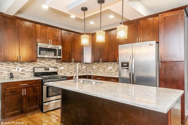 kitchen with hanging light fixtures, sink, appliances with stainless steel finishes, light hardwood / wood-style floors, and light stone counters