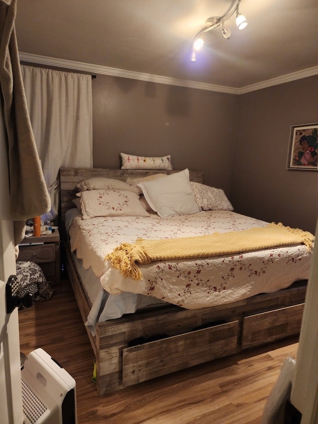 bedroom with wood-type flooring, track lighting, and crown molding