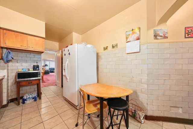 kitchen with light tile patterned flooring, white fridge with ice dispenser, and tile walls