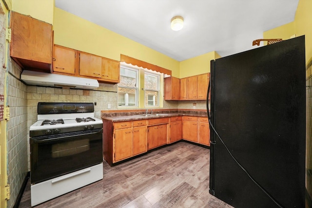 kitchen with gas range gas stove, sink, black fridge, light hardwood / wood-style floors, and decorative backsplash