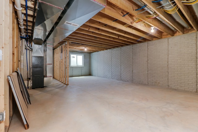 basement featuring brick wall and heating unit