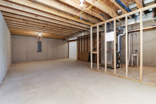 basement featuring electric panel, heating unit, and brick wall