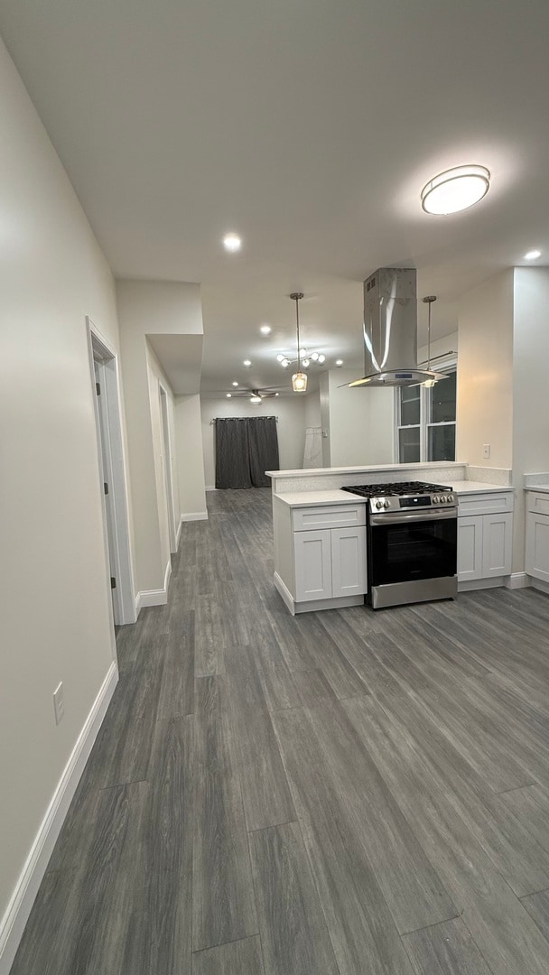 kitchen with dark wood-type flooring, island range hood, white cabinets, kitchen peninsula, and stainless steel range with gas cooktop