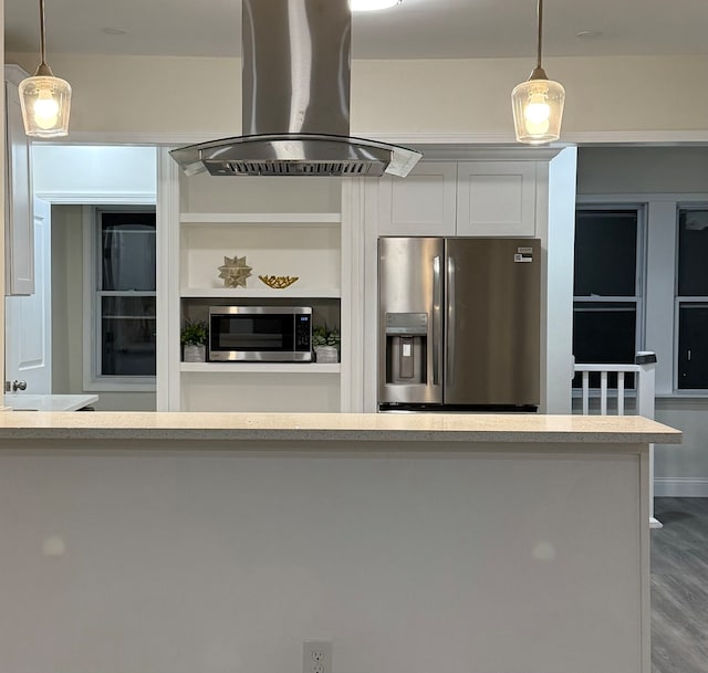 kitchen featuring appliances with stainless steel finishes, wall chimney exhaust hood, hanging light fixtures, wood-type flooring, and white cabinets