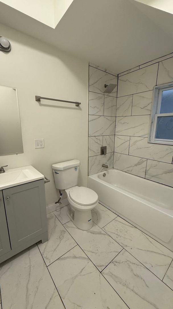 full bathroom featuring vanity, tiled shower / bath, and toilet