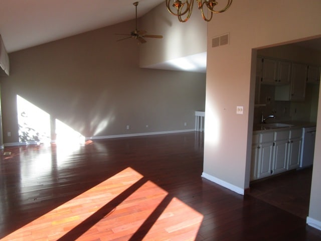 unfurnished living room featuring high vaulted ceiling, ceiling fan with notable chandelier, sink, and dark hardwood / wood-style flooring