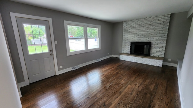 unfurnished living room with a brick fireplace, dark hardwood / wood-style floors, and a healthy amount of sunlight