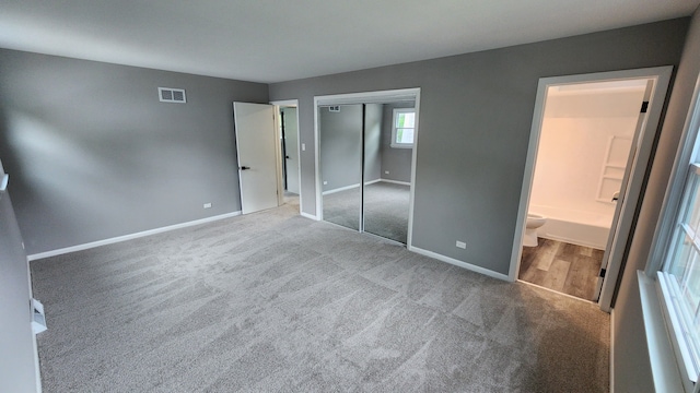 unfurnished bedroom with carpet floors, baseboards, a closet, and ensuite bath