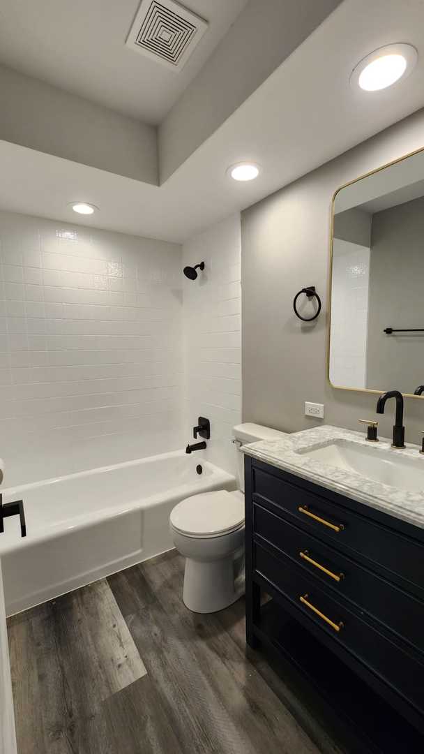 full bathroom featuring toilet, tiled shower / bath combo, vanity, and wood-type flooring