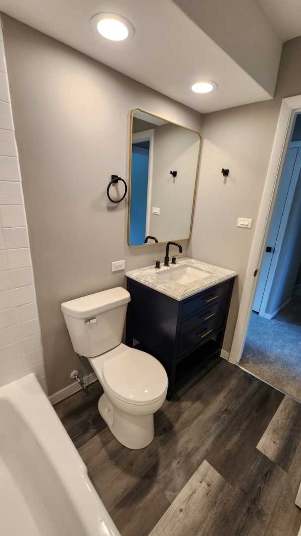 full bath with wood finished floors, toilet, vanity, a tub, and recessed lighting