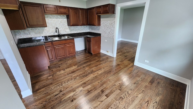 kitchen featuring dark wood-type flooring, decorative backsplash, sink, and dark stone countertops