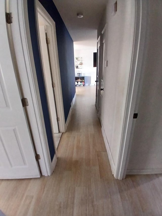 corridor with light wood-type flooring and baseboards