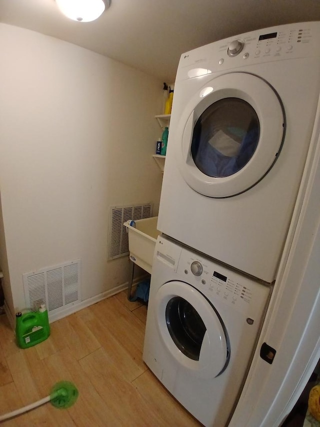washroom featuring stacked washer / drying machine, light wood-type flooring, and baseboards