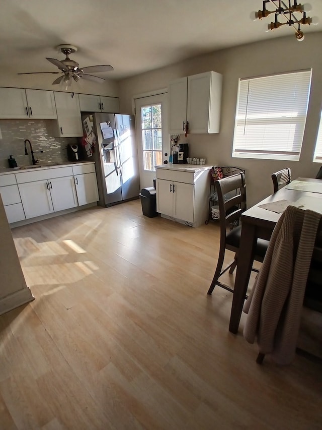 kitchen featuring stainless steel refrigerator with ice dispenser, decorative backsplash, ceiling fan, white cabinetry, and light wood-type flooring