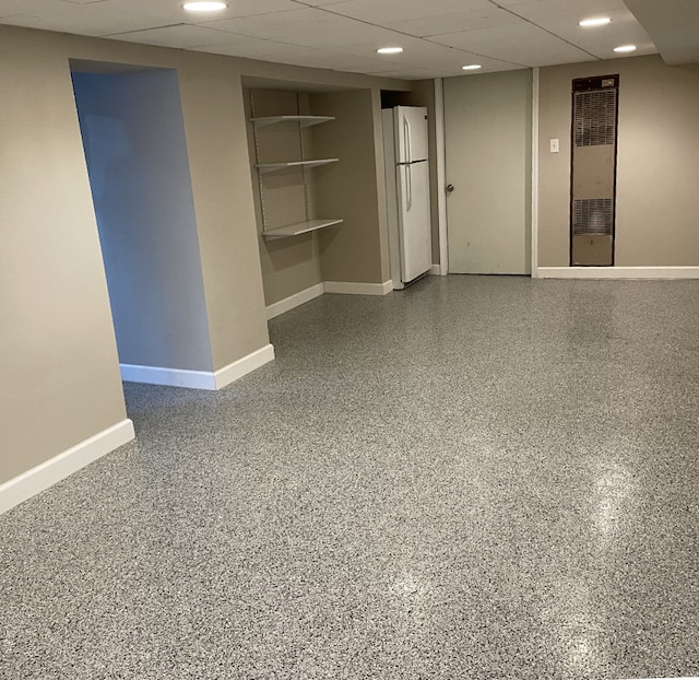 basement featuring a drop ceiling and white fridge