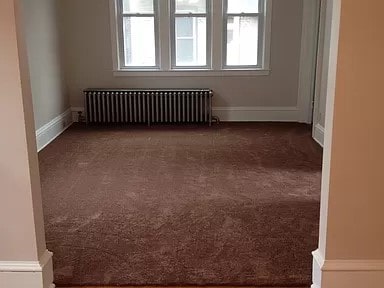 empty room with radiator, dark carpet, and a healthy amount of sunlight