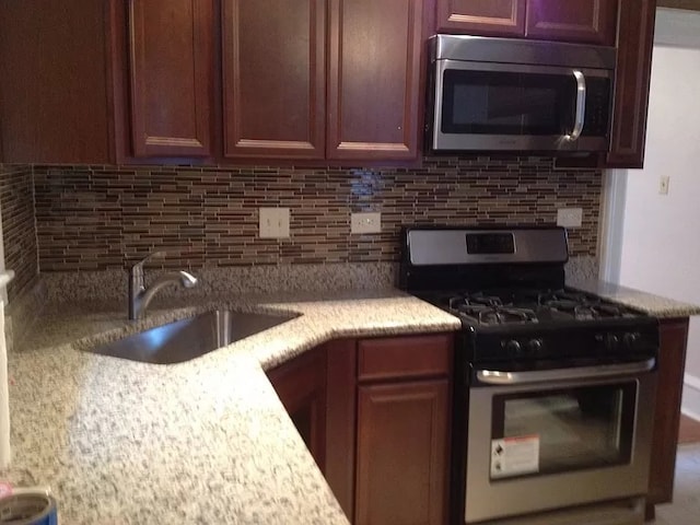 kitchen with decorative backsplash, sink, light stone counters, and appliances with stainless steel finishes