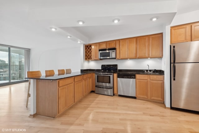 kitchen featuring kitchen peninsula, appliances with stainless steel finishes, a kitchen bar, and light wood-type flooring