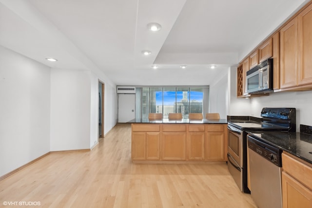 kitchen featuring stainless steel appliances, dark stone counters, kitchen peninsula, light hardwood / wood-style flooring, and a wall mounted air conditioner