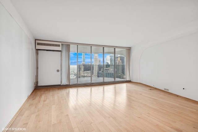 unfurnished room featuring light hardwood / wood-style floors, a wall mounted AC, and floor to ceiling windows