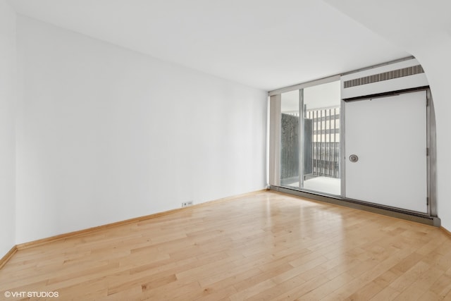 spare room with a wall of windows and light hardwood / wood-style floors