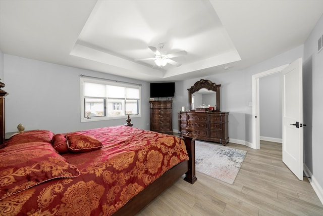 bedroom with a raised ceiling, light hardwood / wood-style flooring, and ceiling fan