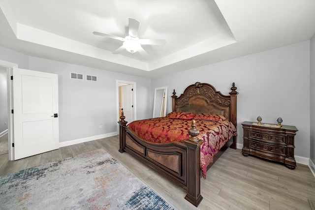 bedroom featuring light hardwood / wood-style floors, a raised ceiling, and ceiling fan