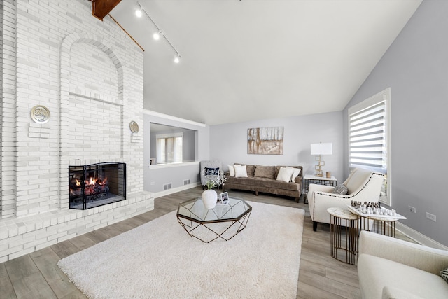 living room featuring a fireplace, rail lighting, hardwood / wood-style flooring, and vaulted ceiling