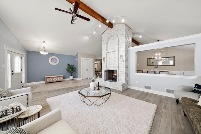 living room with beamed ceiling, track lighting, a fireplace, ceiling fan with notable chandelier, and hardwood / wood-style flooring