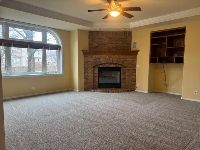 unfurnished living room with ornamental molding, a brick fireplace, a raised ceiling, and baseboards