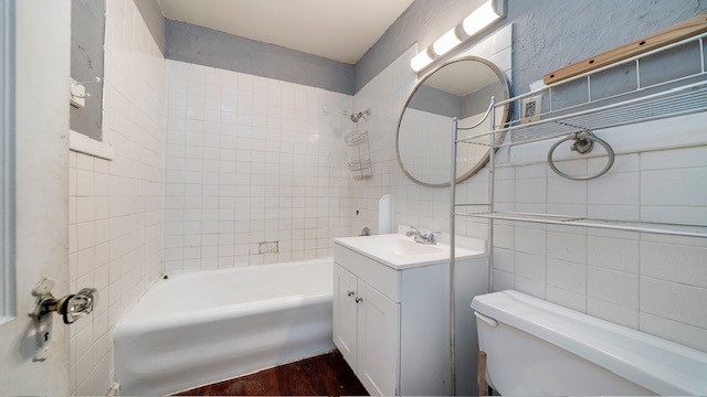 full bathroom with toilet, tile walls, hardwood / wood-style flooring, tiled shower / bath combo, and vanity