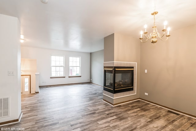 unfurnished living room featuring hardwood / wood-style floors, a multi sided fireplace, and a chandelier