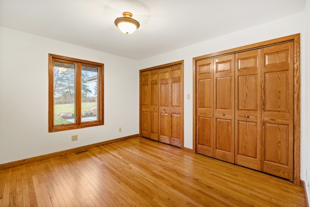 unfurnished bedroom with light wood-type flooring and multiple closets