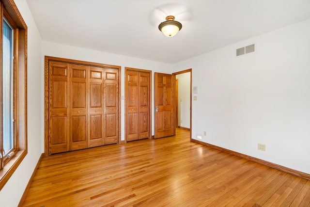 unfurnished bedroom featuring two closets, light hardwood / wood-style floors, and multiple windows