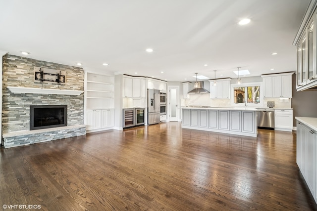 unfurnished living room featuring built in features, wine cooler, a stone fireplace, and dark wood-type flooring