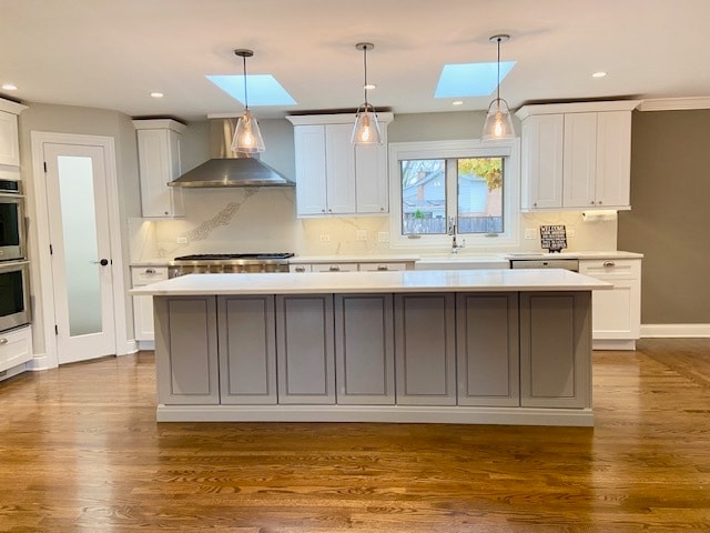 kitchen featuring a kitchen island, wall chimney range hood, dark wood-type flooring, and a skylight