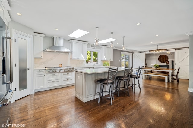 kitchen featuring white cabinets, a barn door, a center island, and wall chimney exhaust hood