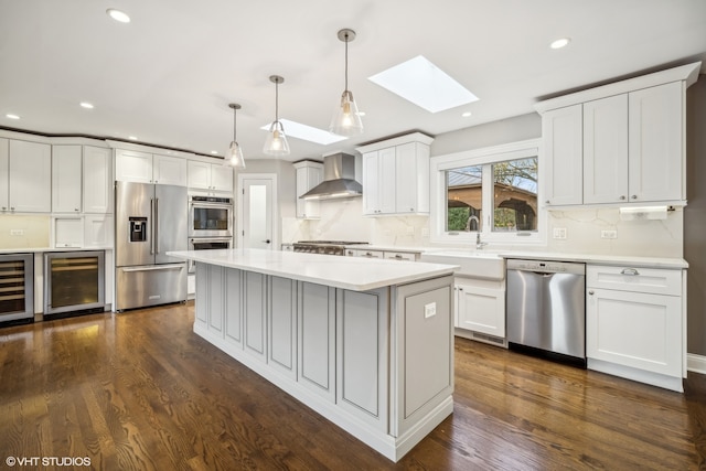 kitchen with dark wood-type flooring, wall chimney range hood, pendant lighting, white cabinets, and appliances with stainless steel finishes