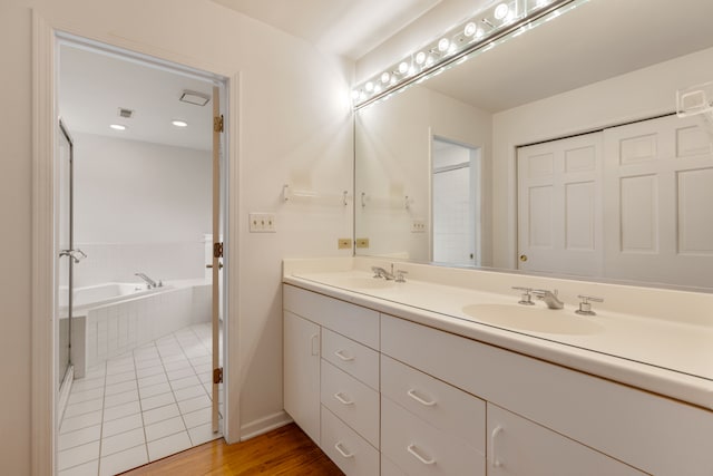 bathroom with hardwood / wood-style flooring, vanity, and tiled bath