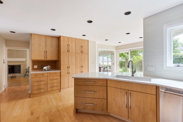 kitchen with sink, tasteful backsplash, light hardwood / wood-style flooring, a brick fireplace, and dishwasher