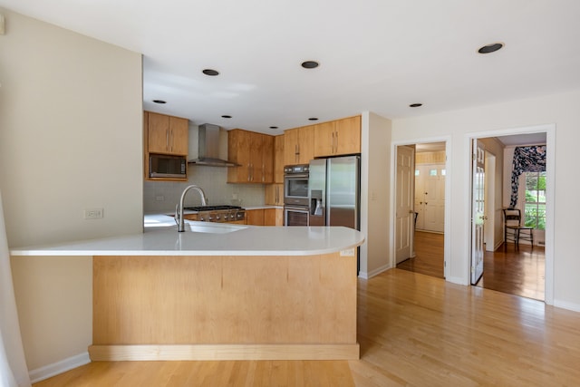 kitchen featuring kitchen peninsula, wall chimney exhaust hood, light hardwood / wood-style flooring, sink, and appliances with stainless steel finishes