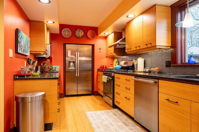 kitchen featuring light wood-type flooring, appliances with stainless steel finishes, decorative backsplash, and wall chimney exhaust hood