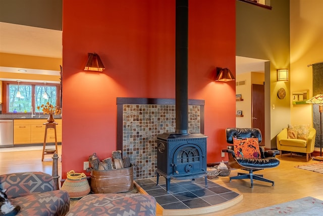 living room featuring a wood stove, hardwood / wood-style floors, a towering ceiling, and sink