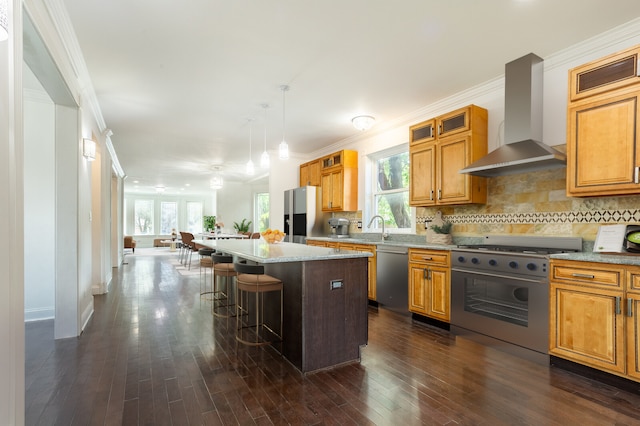 kitchen featuring dark hardwood / wood-style flooring, wall chimney exhaust hood, a kitchen breakfast bar, a kitchen island, and appliances with stainless steel finishes