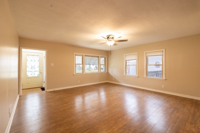 unfurnished room with a textured ceiling, dark wood-type flooring, a healthy amount of sunlight, and ceiling fan