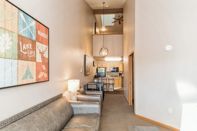 carpeted living room with a towering ceiling, beamed ceiling, and ceiling fan