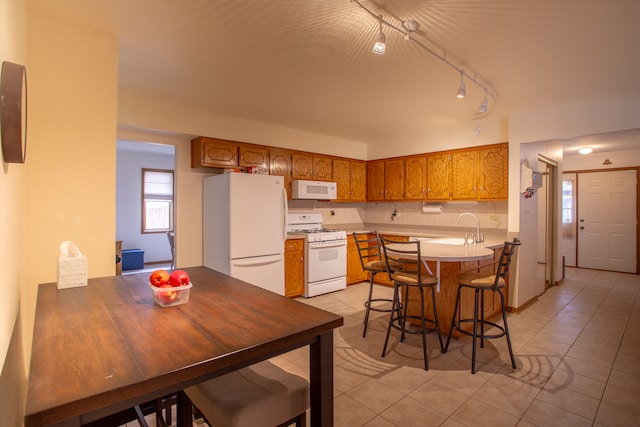 kitchen with white appliances, light tile patterned floors, sink, a breakfast bar, and kitchen peninsula