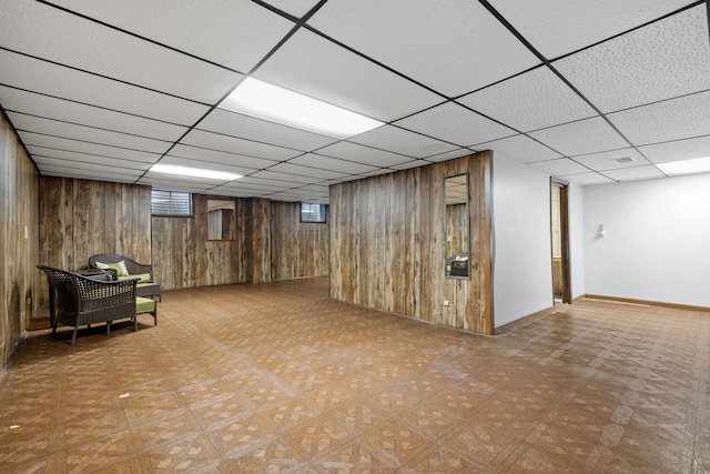 basement featuring a drop ceiling and wooden walls