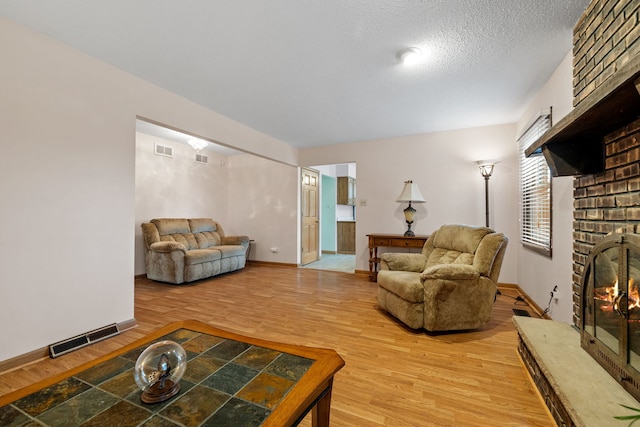 living room with wood-type flooring, a textured ceiling, and a brick fireplace